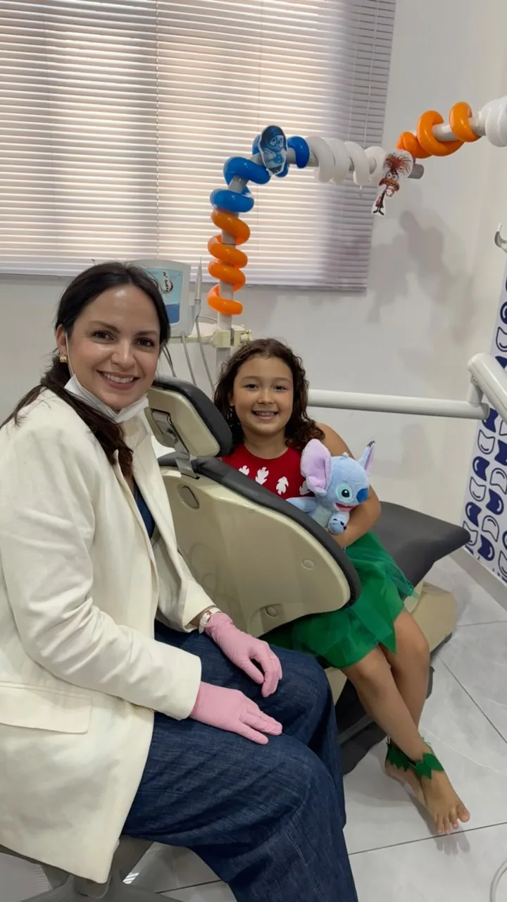 Dentista da Dentalkids sorrindo ao lado de uma menina sentada na cadeira do consultório